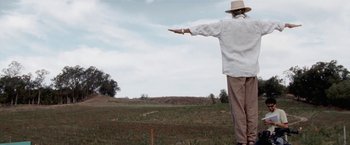 Movie still from “The Biggest Little Farm” (2018), directed by John Chester – A man in a white shirt and a cowboy hat pointing to a field; Wide shot, Low angle