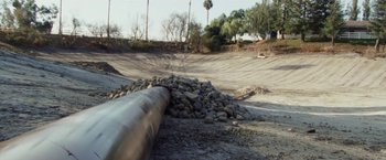 Movie still from “The Biggest Little Farm” (2018), directed by John Chester – A large metal pipe sitting next to a pile of rocks; Extreme Wide shot, High angle