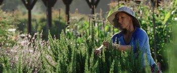 Movie still from “The Biggest Little Farm” (2018), directed by John Chester – A woman in a hat is tending to a plant; Medium shot, Low angle