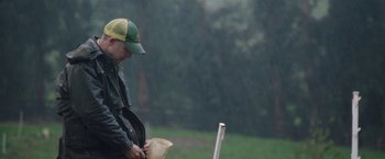 Movie still from “The Biggest Little Farm” (2018), directed by John Chester – A man standing in the pouring rain holding a bucket; Medium shot, Low angle
