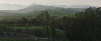 Movie still from “The Biggest Little Farm” (2018), directed by John Chester – A view of a field with trees and mountains in the background; Extreme Wide shot, High angle