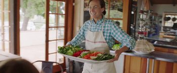 Movie still from “The Biggest Little Farm” (2018), directed by John Chester – A woman holding a tray of vegetables in a kitchen; Medium shot, Low angle