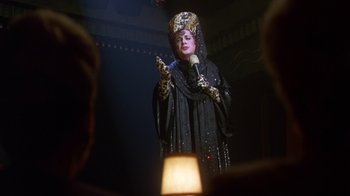 Movie still from “The Birdcage” (1996), directed by Mike Nichols – A woman dressed in a black outfit holding a microphone; Medium shot, Over the shoulder angle