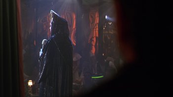 Movie still from “The Birdcage” (1996), directed by Mike Nichols – A man in a black robe and a black hat; Medium shot, Over the shoulder angle