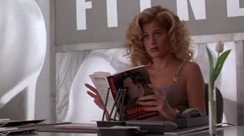 Movie still from “The Birdcage” (1996), directed by Mike Nichols – A woman sitting at a table reading a magazine; Close Up shot, Low angle