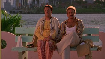 Movie still from “The Birdcage” (1996), directed by Mike Nichols – A couple of people sitting on top of a wooden bench; Medium shot, Low angle