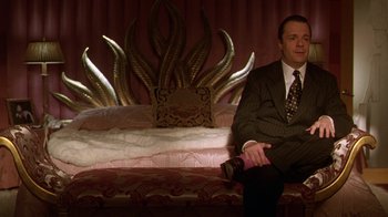 Movie still from “The Birdcage” (1996), directed by Mike Nichols – A man in a suit sitting on top of a bed; Medium shot, Low angle