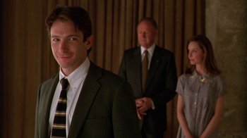 Movie still from “The Birdcage” (1996), directed by Mike Nichols – A man in a suit standing in front of two other people; Close Up shot, Over the shoulder angle