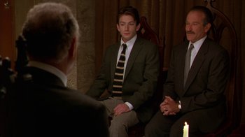 Movie still from “The Birdcage” (1996), directed by Mike Nichols – A man in a suit sitting in front of two other men; Medium shot, Over the shoulder angle