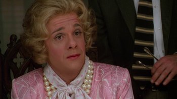 Movie still from “The Birdcage” (1996), directed by Mike Nichols – A man with blonde hair wearing a pink and white dress and pearls; Close Up shot, Over the shoulder angle