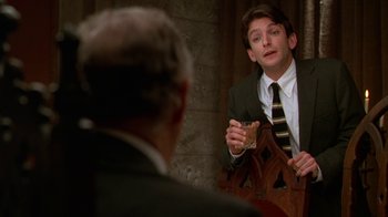 Movie still from “The Birdcage” (1996), directed by Mike Nichols – A man in a suit and tie holding a piece of cake; Medium shot, Over the shoulder angle