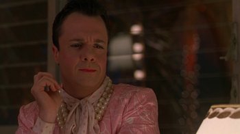 Movie still from “The Birdcage” (1996), directed by Mike Nichols – A man in a pink suit and pearls is sitting in a dimly lit room; Close Up shot, Over the shoulder angle