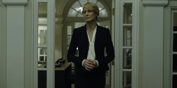 Movie still from “House of Cards” (2013), created by Beau Willimon – A woman in a suit standing in front of a window; Medium shot, Low angle
