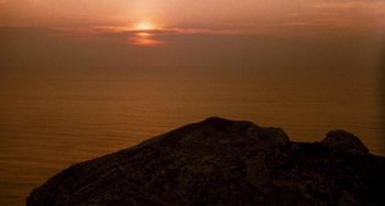 Movie still from “The Black Stallion” (1979), directed by Carroll Ballard – The sun is setting over the ocean with a rock in the foreground; Extreme Wide shot, High angle