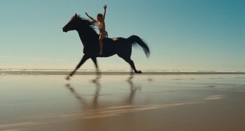Movie still from “The Black Stallion” (1979), directed by Carroll Ballard – A man riding a horse on the beach; Wide shot, Low angle