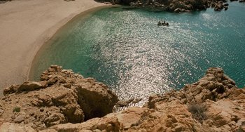 Movie still from “The Black Stallion” (1979), directed by Carroll Ballard – A boat is in the water near the shore of a beach; Extreme Wide shot, Overhead angle