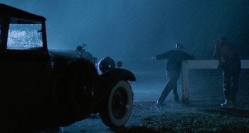 Movie still from “The Black Stallion” (1979), directed by Carroll Ballard – A man standing in the rain next to an antique car; Wide shot, Low angle