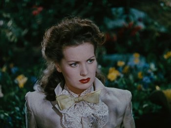 Movie still from “The Black Swan” (1942), directed by Henry King – A woman with a bow tie in front of flowers; Close Up shot, Over the shoulder angle