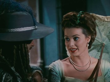 Movie still from “The Black Swan” (1942), directed by Henry King – A woman in a hat and pearls talking to a man in a hat; Close Up shot, Over the shoulder angle