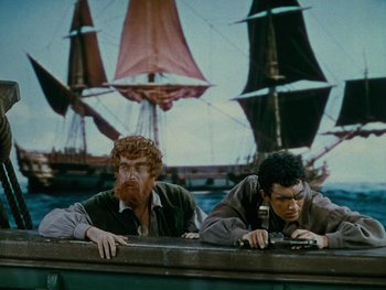 Movie still from “The Black Swan” (1942), directed by Henry King – Two men sitting at a table in front of a ship; Medium shot, Low angle