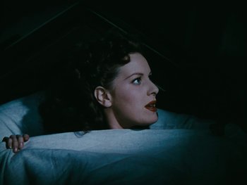 Movie still from “The Black Swan” (1942), directed by Henry King – A woman with dark hair and red lipstick is laying in a bed; Close Up shot, Overhead angle