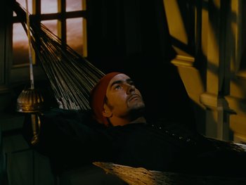 Movie still from “The Black Swan” (1942), directed by Henry King – A man laying in a hammock in a dark room; Medium shot, High angle