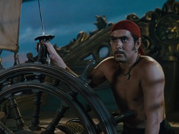 Movie still from “The Black Swan” (1942), directed by Henry King – A shirtless man sitting in front of a steering wheel on a boat; Medium shot, High angle