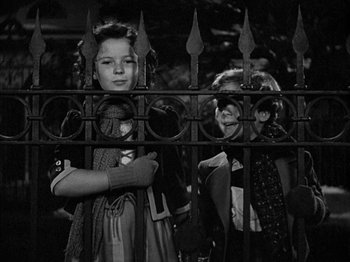 Movie still from “The Blue Bird” (1940), directed by Walter Lang – Two young girls standing next to each other behind an iron fence; Medium shot, High angle