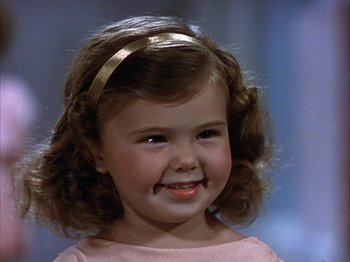 Movie still from “The Blue Bird” (1940), directed by Walter Lang – A little girl with brown curly hair wearing a pink dress; Close Up shot, High angle