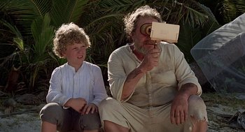 Movie still from “The Blue Lagoon” (1980), directed by Randal Kleiser – An older man and a young boy sitting next to each other; Medium shot, High angle