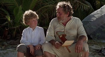 Movie still from “The Blue Lagoon” (1980), directed by Randal Kleiser – An older man sitting next to a young boy; Medium shot, High angle