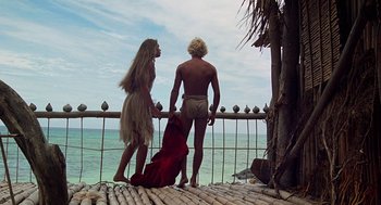 Movie still from “The Blue Lagoon” (1980), directed by Randal Kleiser – A man and a woman standing next to a railing on the beach; Wide shot, Low angle