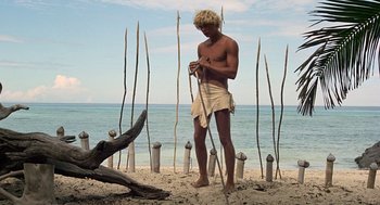 Movie still from “The Blue Lagoon” (1980), directed by Randal Kleiser – A man standing on the beach holding a stick; Wide shot, Low angle