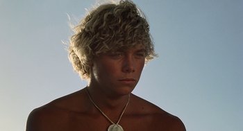 Movie still from “The Blue Lagoon” (1980), directed by Randal Kleiser – A young man with blonde hair wearing a necklace; Close Up shot, Low angle
