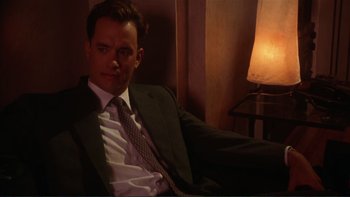 Movie still from “The Bonfire of the Vanities” (1990), directed by Brian De Palma – A man in a suit and tie sitting in front of a lamp; Medium shot, Low angle