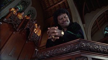 Movie still from “The Bonfire of the Vanities” (1990), directed by Brian De Palma – A man sitting in a chair with his hands clasped together; Medium shot, Low angle