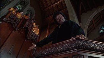 Movie still from “The Bonfire of the Vanities” (1990), directed by Brian De Palma – A man standing in front of an organ in a church; Medium shot, Low angle