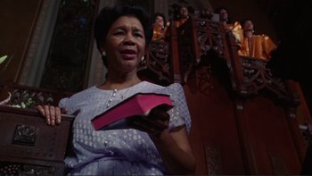 Movie still from “The Bonfire of the Vanities” (1990), directed by Brian De Palma – An older woman holding a pink box in her hands; Medium shot, Low angle