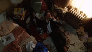 Movie still from “The Bonfire of the Vanities” (1990), directed by Brian De Palma – A man is laying on the floor in a messy room; Wide shot, Overhead angle