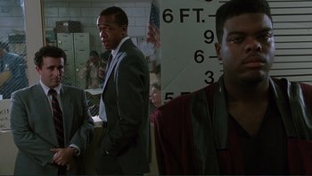 Movie still from “The Bonfire of the Vanities” (1990), directed by Brian De Palma – A man in a gray suit standing next to a man in a red jacket; Medium shot, Over the shoulder angle