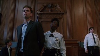 Movie still from “The Bonfire of the Vanities” (1990), directed by Brian De Palma – A man and a police officer standing in front of a wooden wall; Medium shot, Low angle