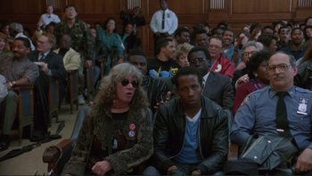 Movie still from “The Bonfire of the Vanities” (1990), directed by Brian De Palma – A group of people sitting in front of a crowd; Medium shot, High angle