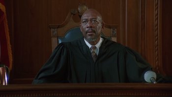 Movie still from “The Bonfire of the Vanities” (1990), directed by Brian De Palma – A man in a judge's robe sitting in a chair; Medium shot, Low angle