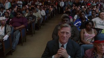 Movie still from “The Bonfire of the Vanities” (1990), directed by Brian De Palma – A crowd of people sitting and standing in a room; Medium shot, High angle