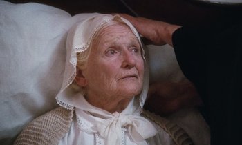 Movie still from “The Bostonians” (1984), directed by James Ivory – An old woman wearing a white dress and a white hat; Close Up shot, High angle