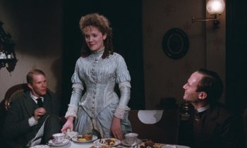 Movie still from “The Bostonians” (1984), directed by James Ivory – A woman standing at a table with a plate of food on top of it; Medium shot, Over the shoulder angle