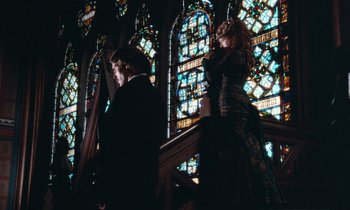 Movie still from “The Bostonians” (1984), directed by James Ivory – A man and a woman standing next to each other in front of a stained glass window; Medium shot, Low angle