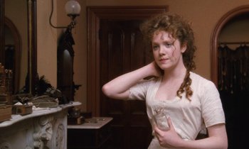 Movie still from “The Bostonians” (1984), directed by James Ivory – A young woman in a white dress is standing in front of a fireplace; Medium shot, High angle