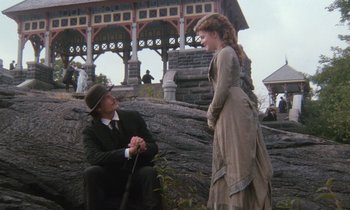 Movie still from “The Bostonians” (1984), directed by James Ivory – A man kneeling next to a woman in front of a building; Wide shot, Low angle