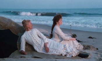 Movie still from “The Bostonians” (1984), directed by James Ivory – Two people sitting on the beach near the ocean; Wide shot, High angle